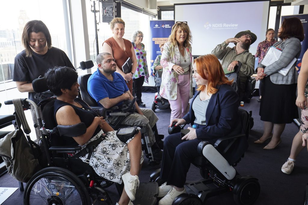 A group of people, some in wheelchairs, are in a group having a chat.