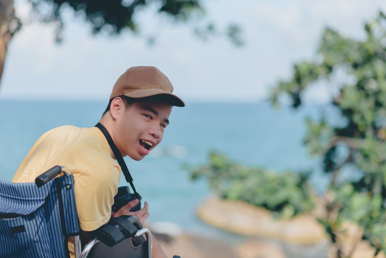 A young man with disability in a wheelchair looking back towards the camera looking happy.