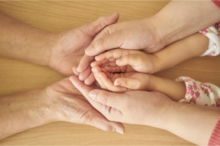 Male and female adult hands are upturned, nesting the hands of a child